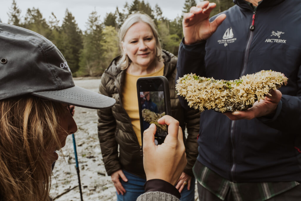 A woman photographs marine life with her phone as another woman looks on